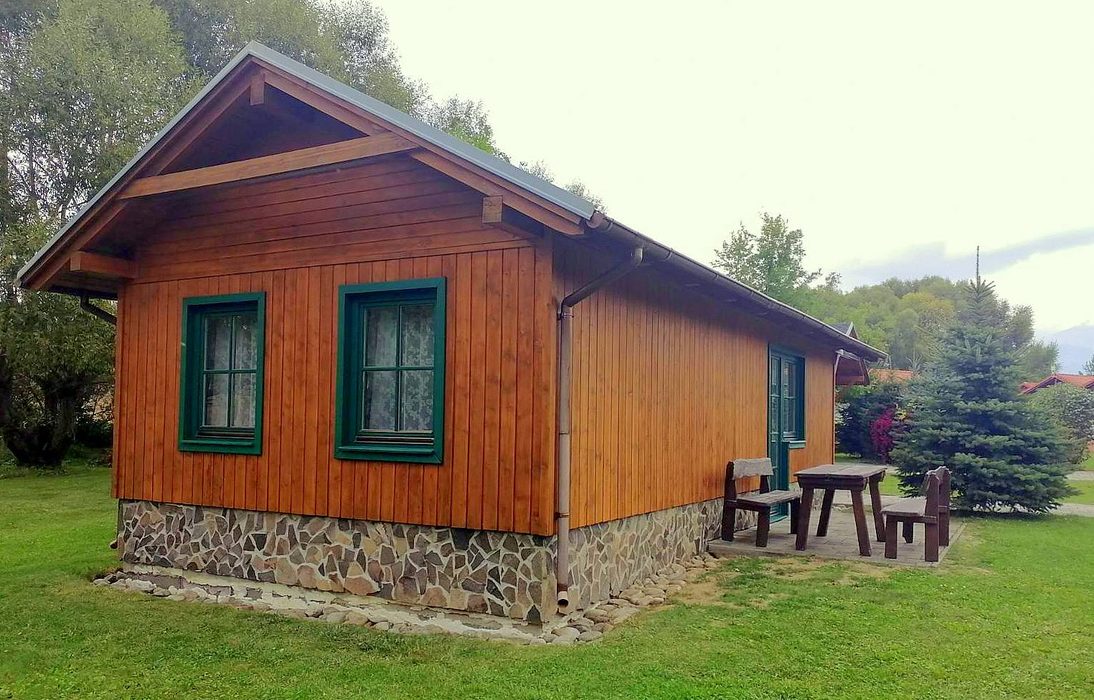 Drevenica so zelenými oknami a dreveným posedením v areáli